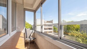 Un balcon avec une chaise, de grandes fenêtres et une vue sur les immeubles et les arbres.
