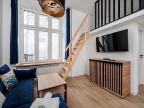 Ein modernes Wohnzimmer mit einer Couch, einem Tisch, einem Fernseher, einer Holzleiter und einem Fenster mit Vorhängen.