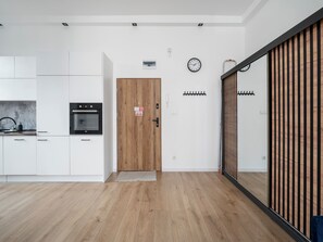 Eine moderne Küche mit weißen Schränken, einer Holztür und einer Uhr an der Wand.