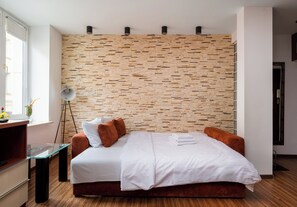 A modern hotel room with a wooden wall, a bed with white linens, a bedside table, and a floor lamp. - Bednarska Royal Route Apartment (Warszawa)