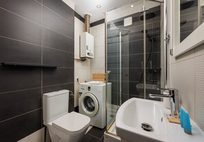 A modern bathroom with a toilet, washing machine, glass shower enclosure, and a sink. - Bednarska Royal Route Apartment (Warszawa)