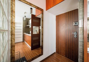 Ein Flur mit einer Holztür, einem Spiegel der eine Küche widerspiegelt und einem kleinen Metallstuhl.