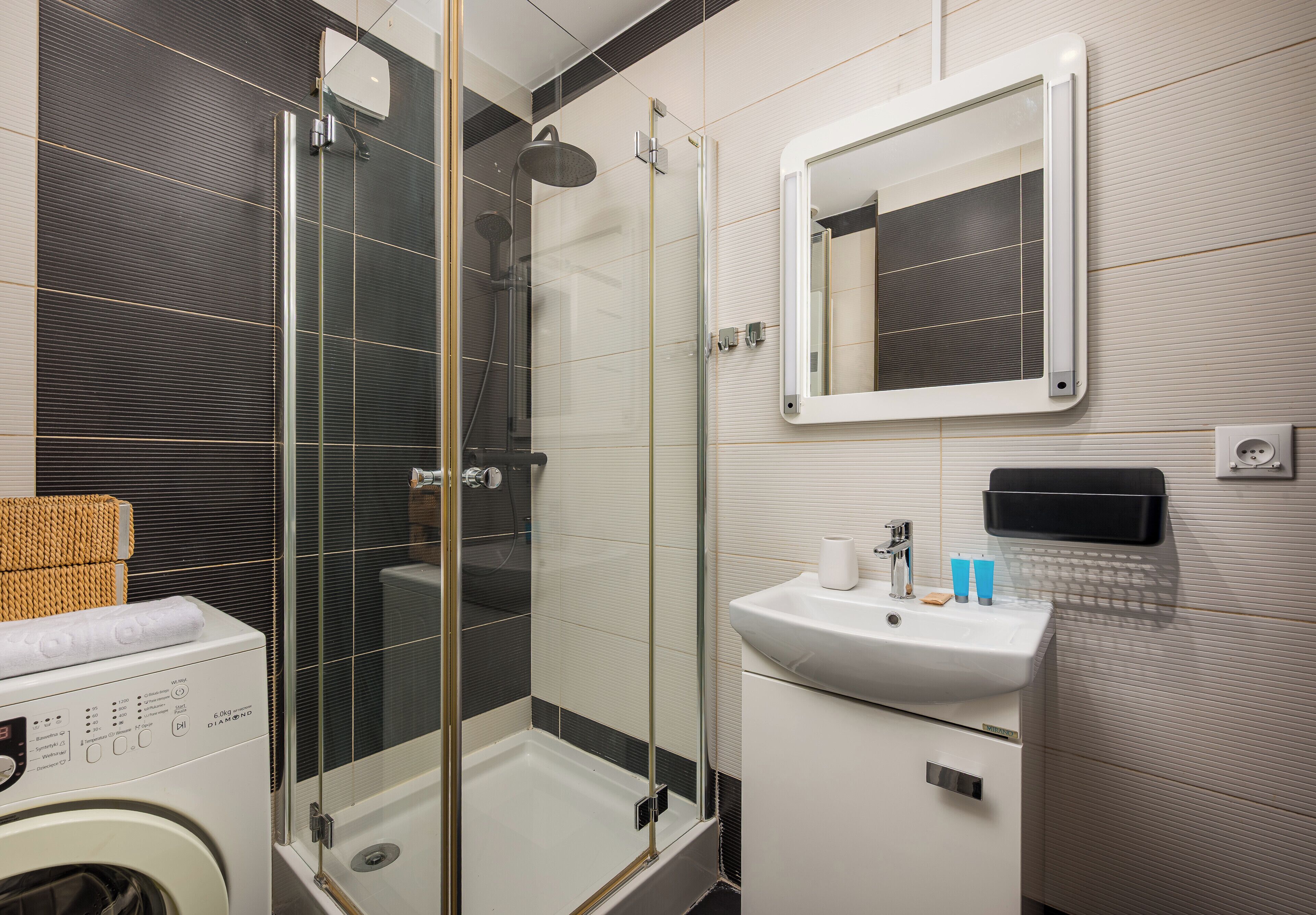 A modern bathroom with a glass-enclosed shower, a sink with a mirror, and a washing machine.