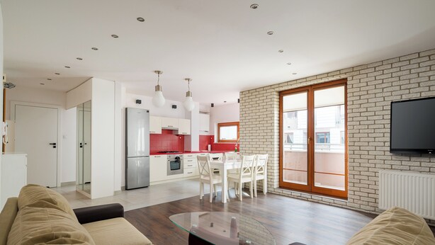 A modern living room with a glass coffee table, a sofa, and a dining area with a red kitchen in the background. - Park Praski Homely Apartment (Warszawa)