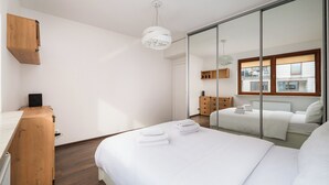 A modern hotel room with a large bed, a wooden dresser, a mirror, and a view of the city. - Park Praski Homely Apartment (Warszawa)