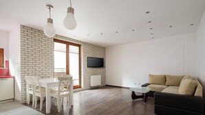 A modern living room with a dining area, a flat-screen TV mounted on the wall, and a sofa. - Park Praski Homely Apartment (Warszawa)