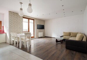 Un soggiorno moderno con zona pranzo, TV a schermo piatto montata a parete e divano.