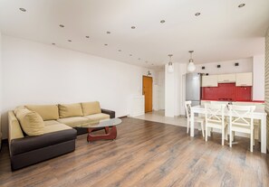 A modern living room with a sofa, ottoman, and coffee table, a dining area with chairs, and a kitchen with red tiles and white cabinets. - Park Praski Homely Apartment (Warszawa)
