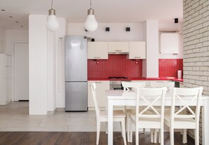 A modern kitchen with white cabinetry, a stainless steel refrigerator, a red tiled backsplash, and a dining area with white chairs. - Park Praski Homely Apartment (Warszawa)
