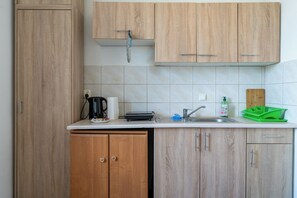 Une cuisine avec des meubles de rangement en bois, une bouilloire, un égouttoir à vaisselle, une assiette verte et un robinet.