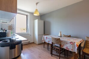 Une cuisine compacte équipée d’un réfrigérateur, d’une table à manger recouverte de nappes à motifs floraux et d’un luminaire suspendu.