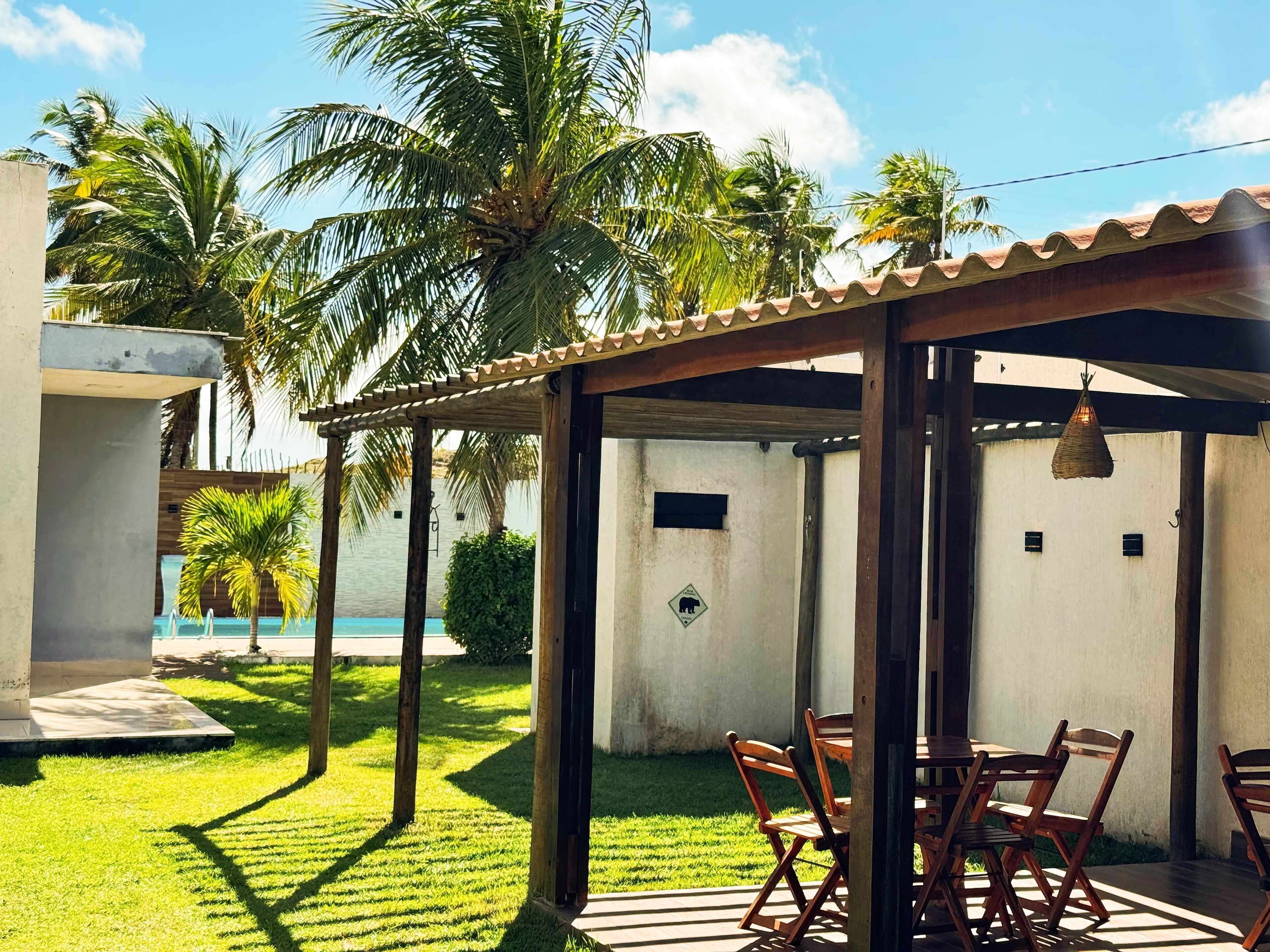 Uma área de estar coberta ao ar livre, com piscina ao fundo.