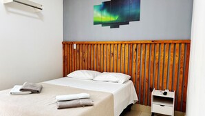 Ein Hotelzimmer mit einem Bett, einem Holzkopfteil, einer Wand-Klimaanlage, einem Nachttisch und einem Bild des Polarlichts.
