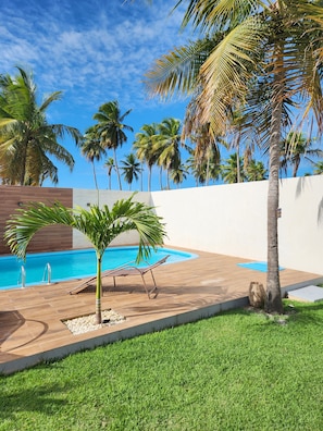 A swimming pool with a lounge chair, palm trees, and a grassy area.