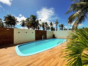 Una piscina amb un pont de fusta, envoltada de palmeres i un cel serè.