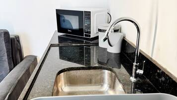 Una kitchenette compacta con microondas, un lavamanos y una cafetera.