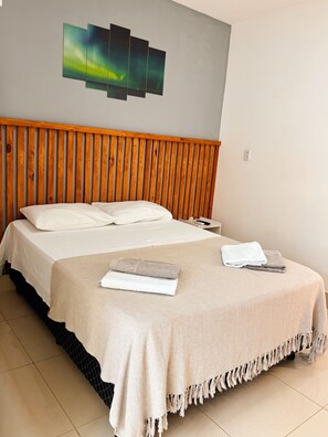 Habitació d'hotel amb un llit, un panell de fusta al capçal, una obra d'art a la paret i un paviment de rajoles.