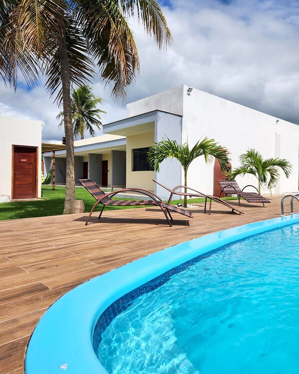 A modern poolside area with a wooden deck, lounge chairs, and a swimming pool.