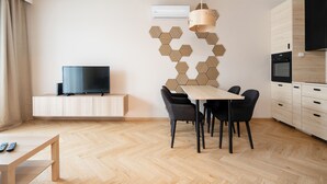 A modern living room with a TV, dining table, chairs, and a kitchen area with an oven.