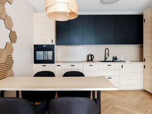 Une cuisine moderne avec une table à manger en bois, des chaises noires et un four encastré.