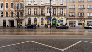 Um edifício de vários andares com estilo arquitetônico clássico, apresentando uma entrada no nível da rua com toldo verde e uma loja visível à direita.