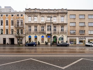 A multi-story building with a classic architectural style, featuring a ground-level entrance with a green awning and a visible shop on the right. - Piotrkowska Cozy Studio (Łódź)