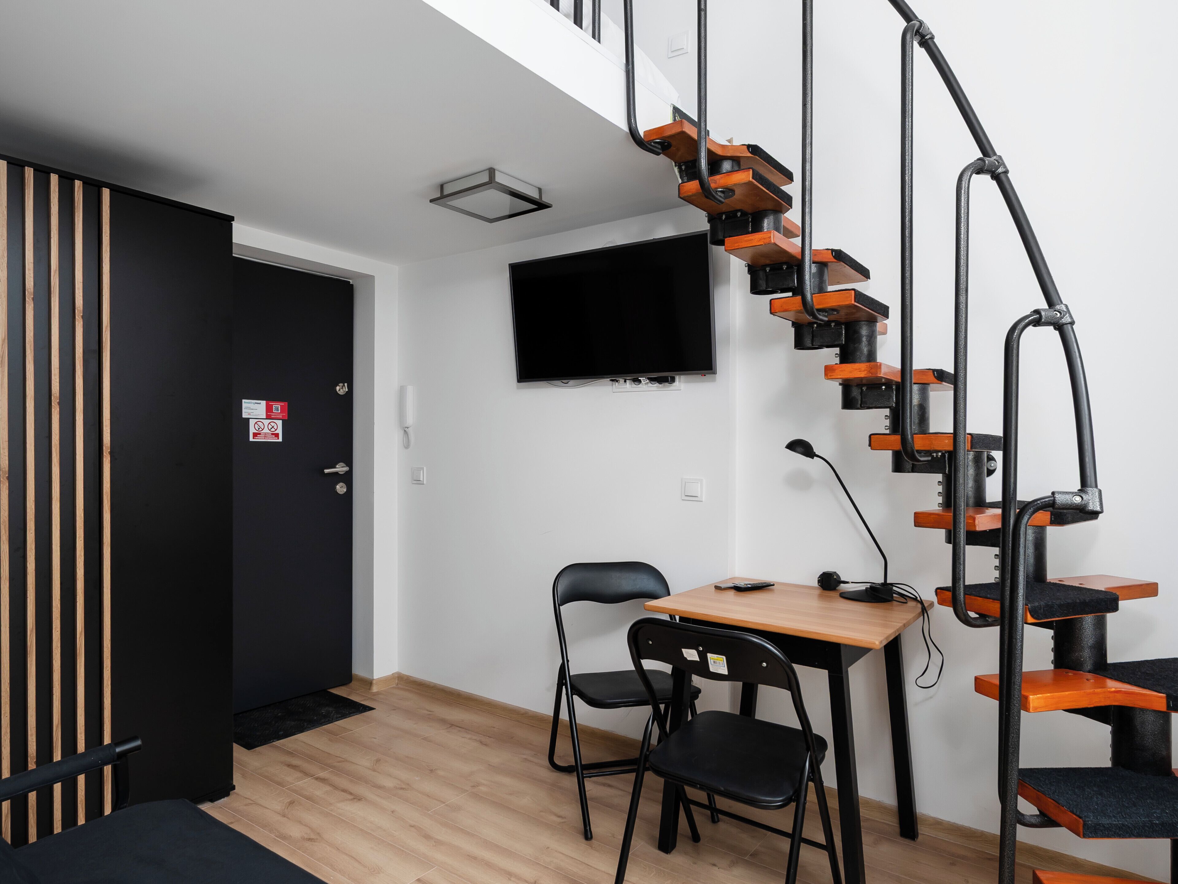 Une pièce avec un plancher en bois, un bureau noir avec une chaise, un canapé noir, une porte noire, un téléviseur noir fixé au mur et un arbre à chat noir.