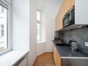 A compact kitchen with a microwave, sink, kettle, and wooden cabinets. - Piotrkowska Cozy Studio (Łódź)