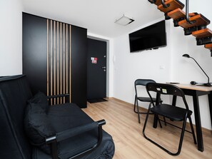 A room with a black sofa, two black chairs, a wooden desk, a black lamp, and a TV mounted on the wall. - Piotrkowska Cozy Studio (Łódź)