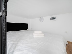 Une chambre à coucher avec un lit, des serviettes blanches, une tête de lit noire, une lampe fixée au mur et une prise de courant.