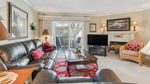 A living room with a leather sofa, a coffee table, a fireplace, and a television. - Coastal St. Simons Retreat | Private Patio + Bonus Suite (Saint Simons Island)