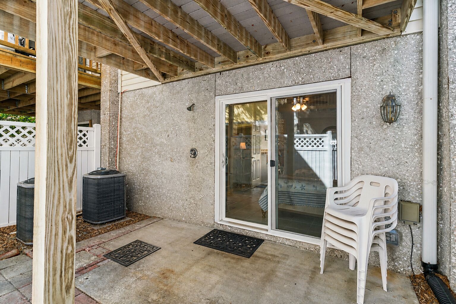 A covered patio with a sliding glass door, outdoor seating, and a white fence.