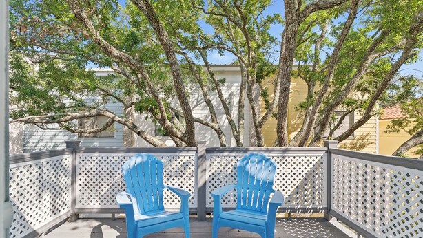 A covered outdoor area with two blue chairs and a white lattice railing. - Coastal St. Simons Retreat | Private Patio + Bonus Suite (Saint Simons Island)