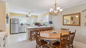 A kitchen with a central island, wooden chairs, a chandelier, and a large mirror on the wall. - Coastal St. Simons Retreat | Private Patio + Bonus Suite (Saint Simons Island)