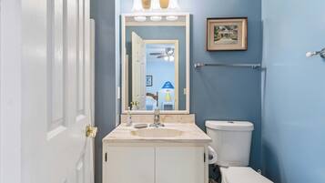 A bathroom with a white sink, a mirror, a toilet, and a framed picture on the wall.