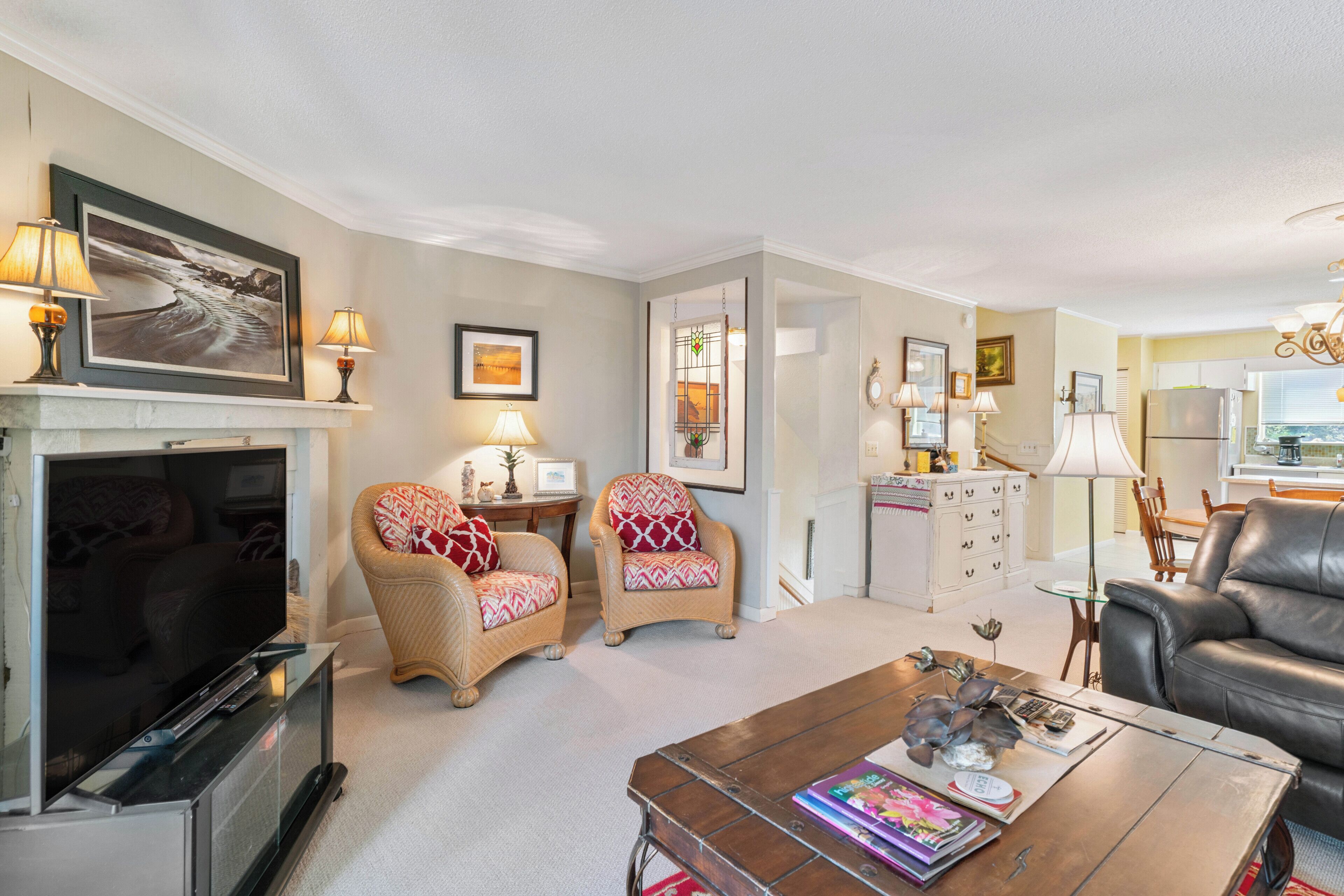 A living room with a fireplace, television, two armchairs, a coffee table with magazines, and a dining area with a table and chairs.