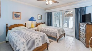 A bedroom with two beds, a ceiling fan, a TV, and a sliding glass door leading to a balcony. - Coastal St. Simons Retreat | Private Patio + Bonus Suite (Saint Simons Island)