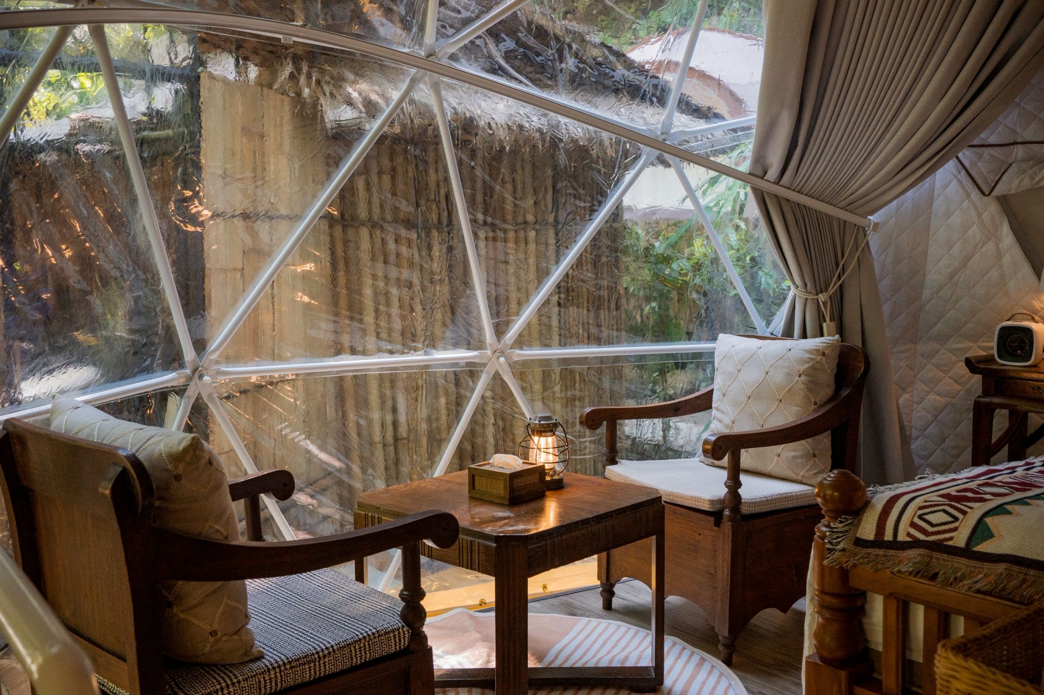 A cozy interior with a large glass dome window, wooden furniture, and a lantern on a table.