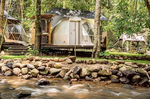 Un campamento con una tienda de campaña, una estructura de madera y un arroyo.