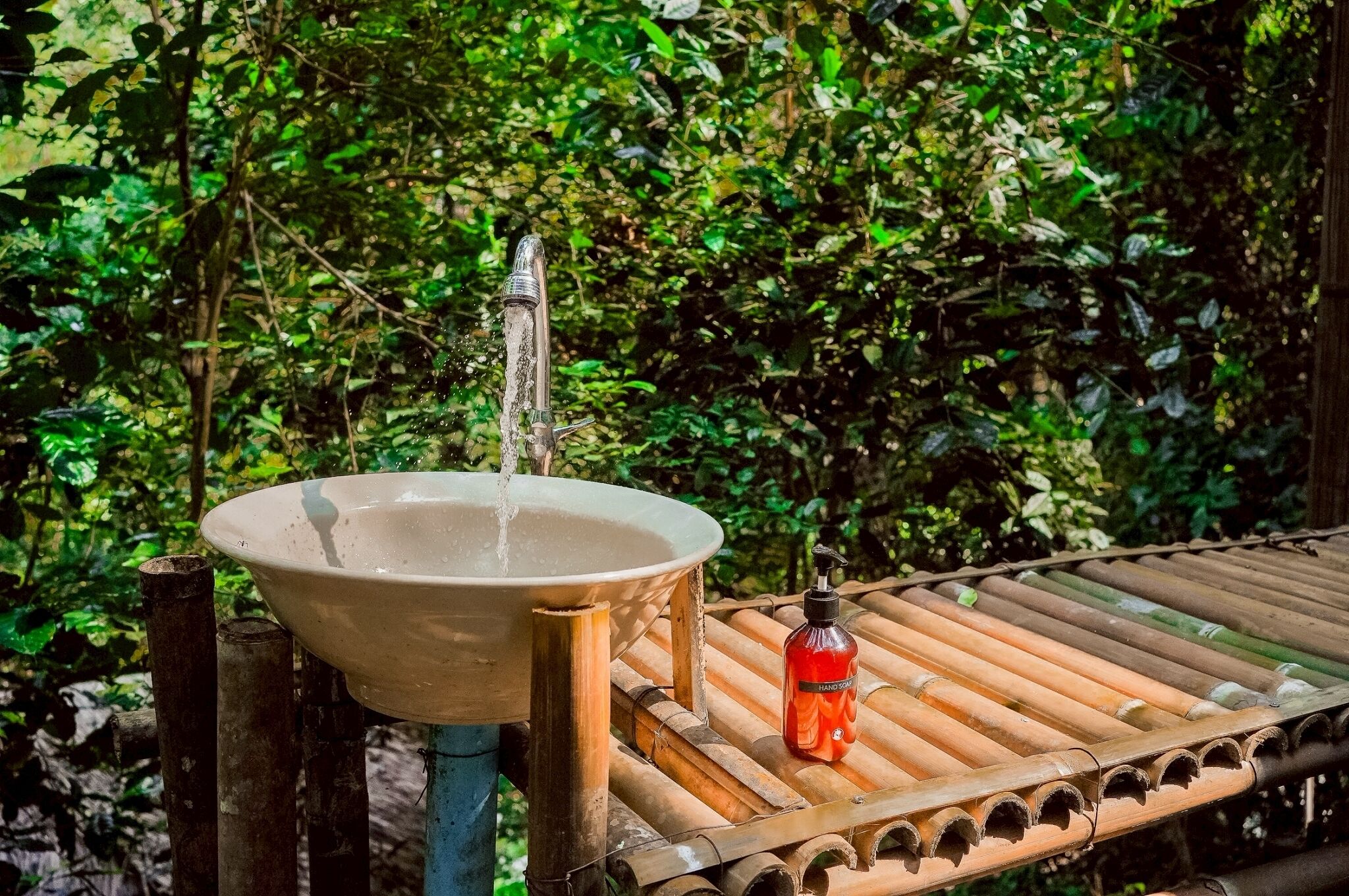 A bamboo lounge chair with a bottle of shampoo, a ceramic sink, and a water spout.
