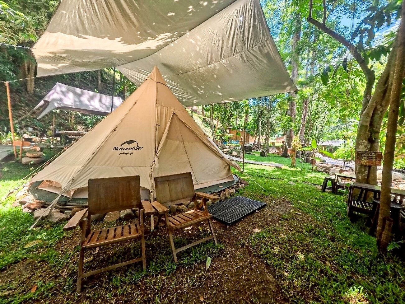 Una carpa Naturehike con una silla de madera y una mesa, rodeada de árboles y follaje.
