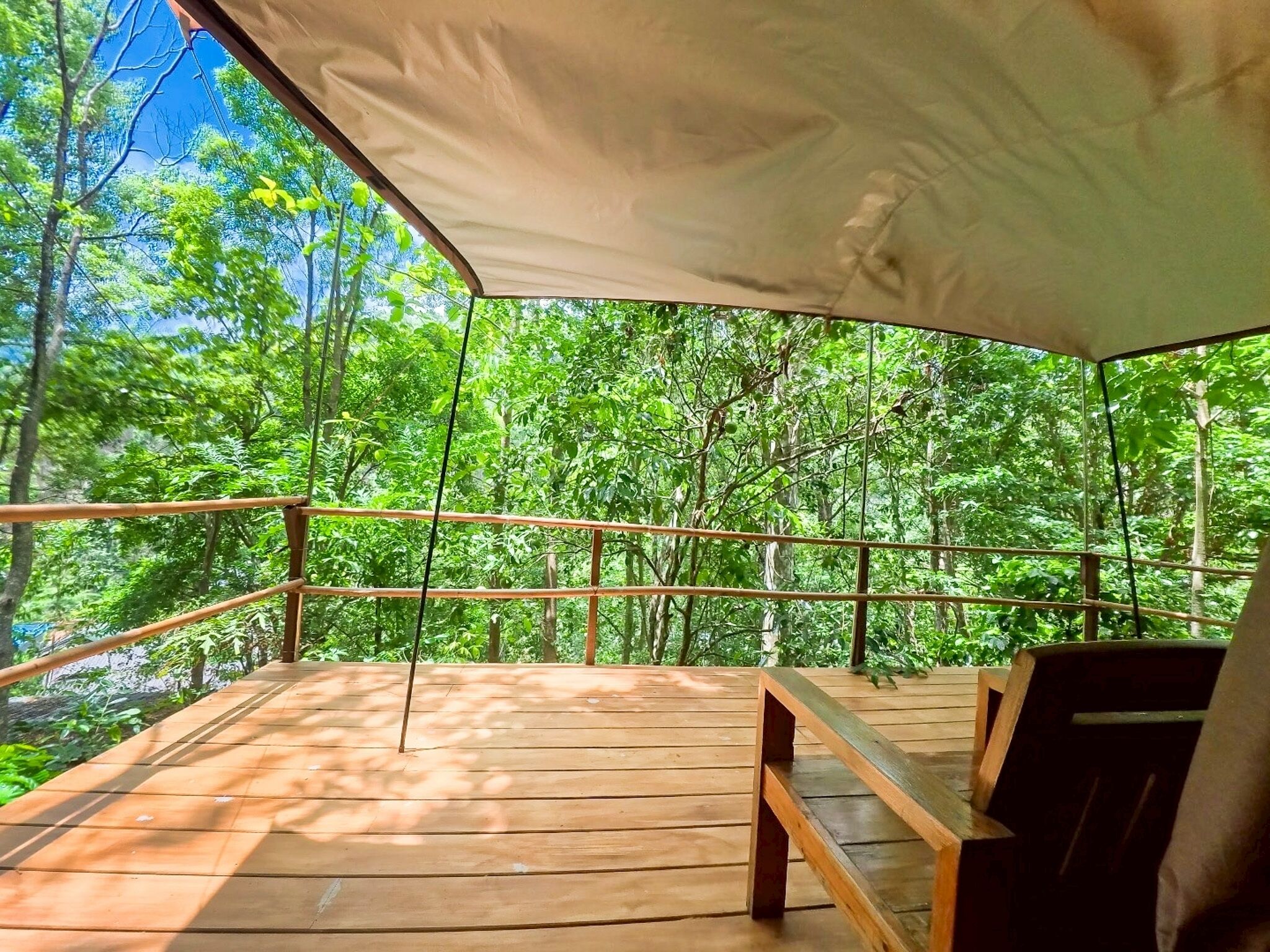 A wooden deck with a railing, a bench, and a canopy providing shade.