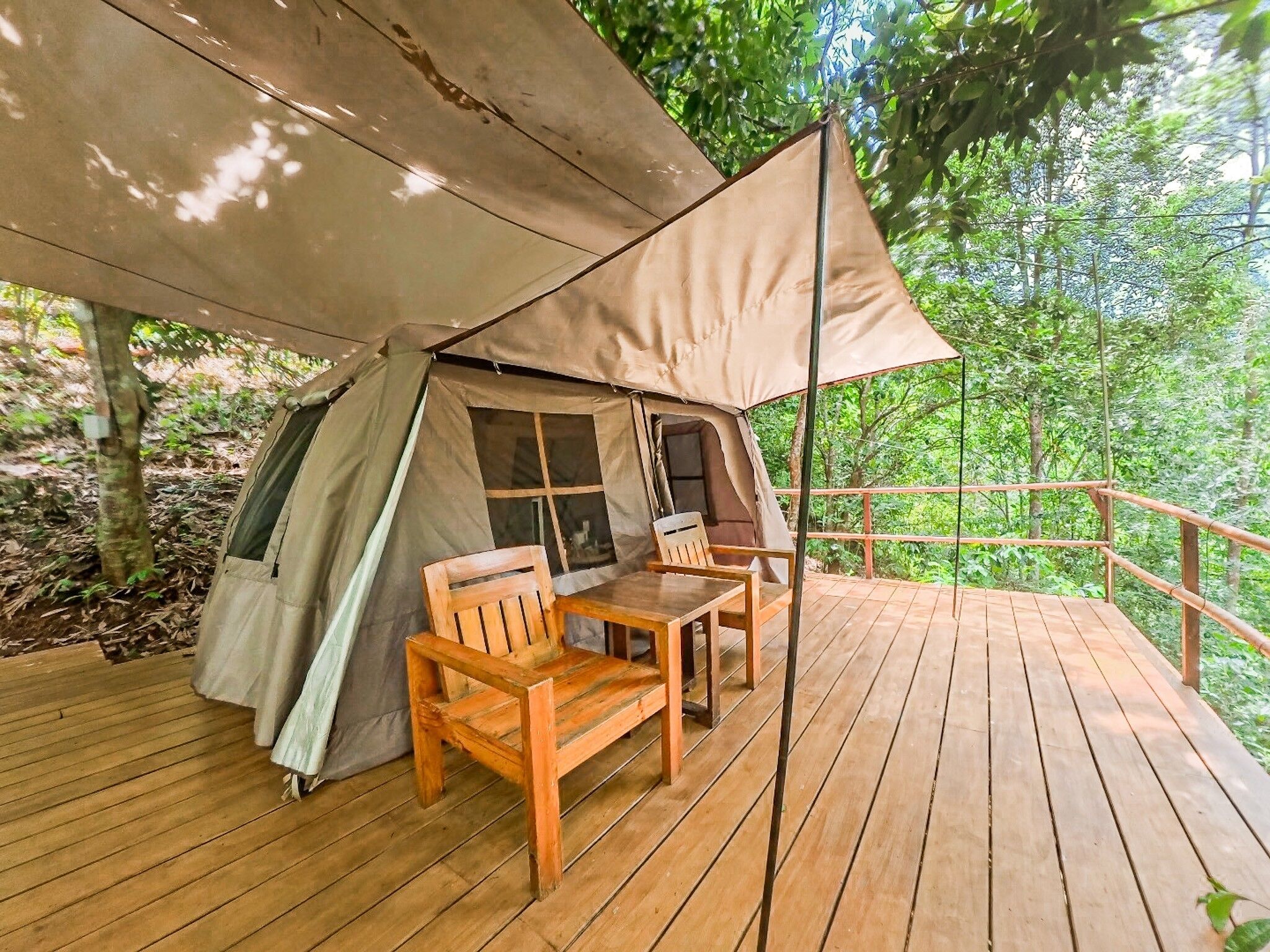 A tent with a table and chairs on a wooden deck surrounded by trees.