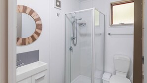 Ein Badezimmer mit einer Duschkabine, einer Toilette, einem Waschbecken mit Spiegel und einem kleinen Teppich.