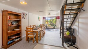 Ein Essbereich mit Holzhockern und einem Tisch, ein Bücherregal und eine Treppe mit Ventilator.