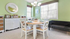 Un coin repas comprenant une table ronde, des chaises blanches, un meuble blanc avec des paniers et un canapé noir.