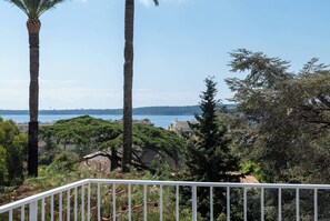 Ein Balkon mit Geländer, der auf eine Küstenlandschaft mit Palmen und Meerblick blickt.