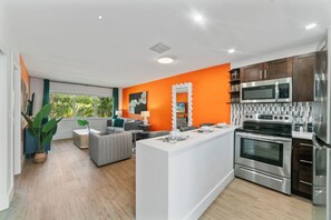 Eine moderne Küche mit Edelstahlgeräten, einer zentralen Kochinsel und einer leuchtend orangefarbenen Akzentwand.