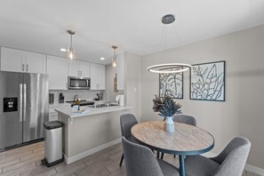 A modern kitchen with stainless steel appliances, a central island, and a dining area with grey chairs and a wooden table. - Minutes to Old Town (Scottsdale)