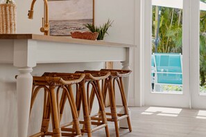 A white bar stool with a woven seat, a white console table with a gold faucet, and a wicker basket.